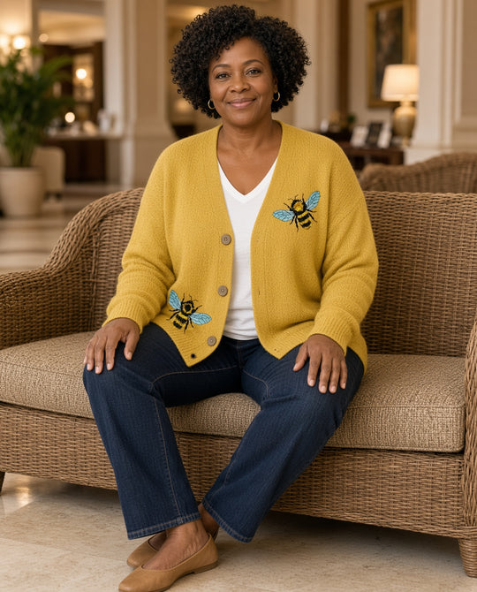 Model seated in a resort lobby wearing the Bee Embroidered Button-Down Cardigan in yellow with dark jeans