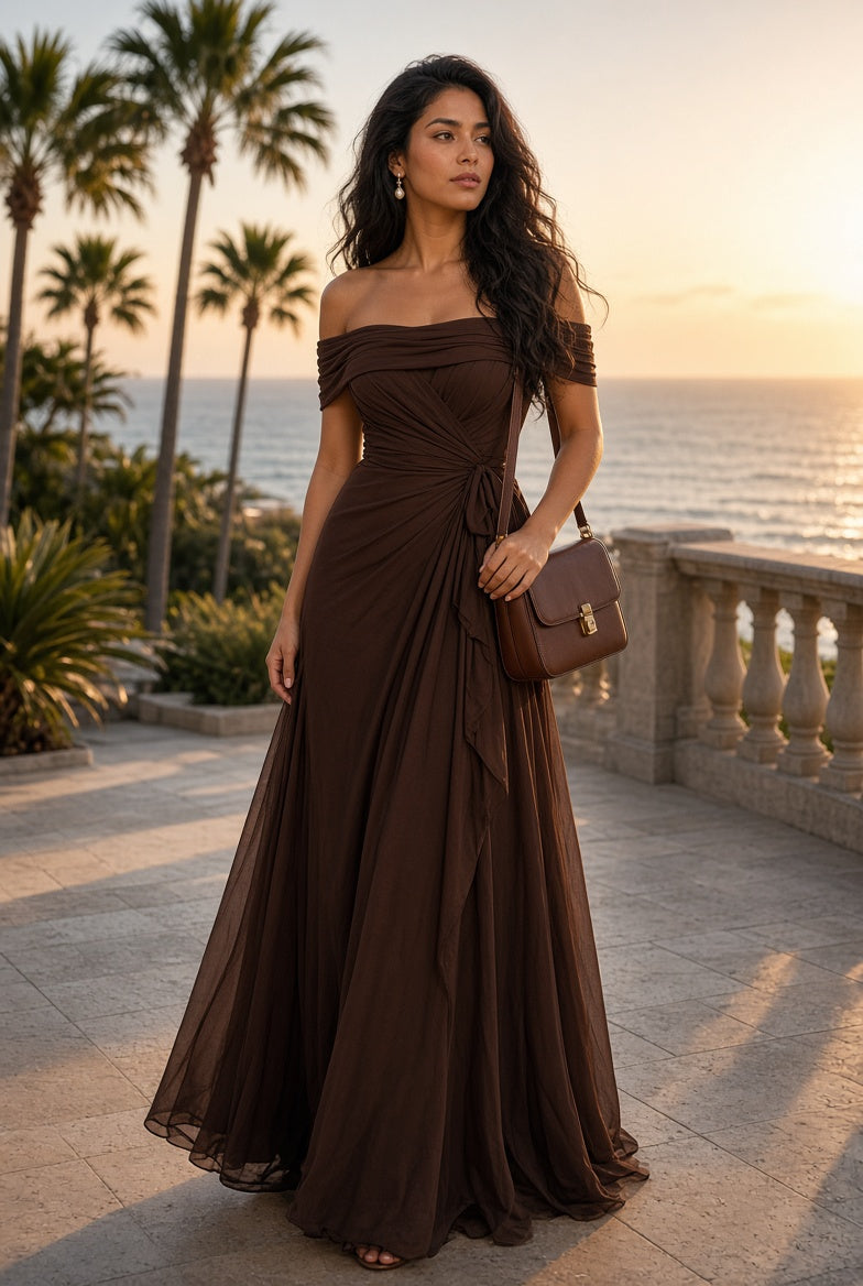 Model wearing the Elara Off-Shoulder Chiffon Maxi Dress in Chocolate on a coastal terrace