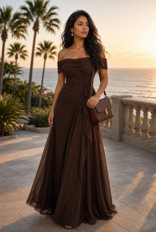 Model wearing the Elara Off-Shoulder Chiffon Maxi Dress in Chocolate on a coastal terrace