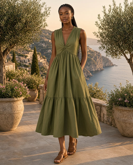 Model wearing the Kalani Twisted V-Neck Tiered Midi Dress in Moss on a cliff-top coastal terrace with olive trees at golden hour